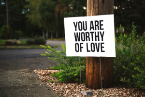 “You are worthy of love,” sign beside tree and road